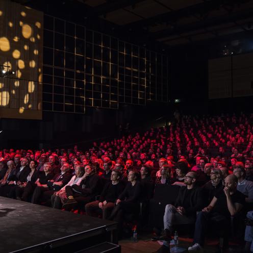 En kvinde står på scenen i Det Kongelige Biblioteks Dronningesal foran publikum.
